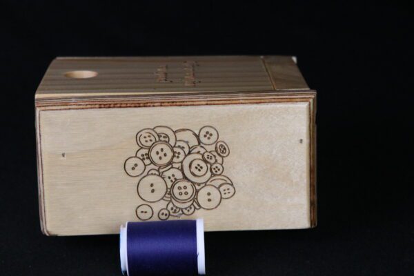 A wooden box with buttons on it and a spool of thread.