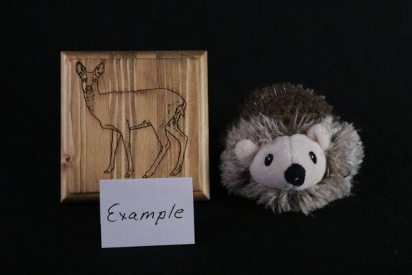 A stuffed animal and wooden picture with an image of a deer.