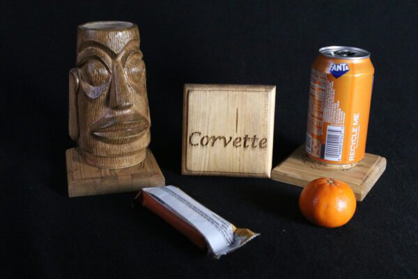 A wooden sculpture of an african head next to a can and orange.