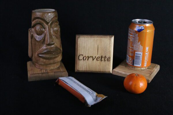 A wooden sculpture of an african head, a can and some orange juice.