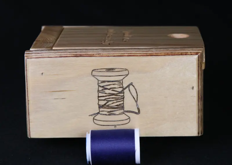 A wooden box with a spool of thread on it.